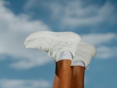 A pair of white running shoes on the end of feet, lifted in the air, in front of a blue sky