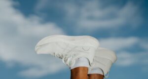 A pair of white running shoes on the end of feet, lifted in the air, in front of a blue sky