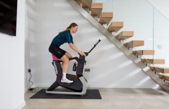 A woman cycles on a stationary bike underneath her stairs.