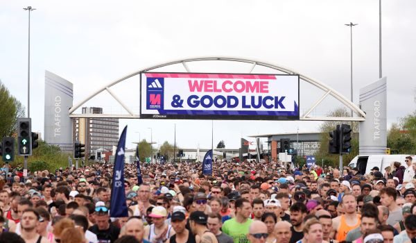 Thosands of runners in the start area of the Manchester Marathon. Banner above tyhem reads Welcome and Good Luck