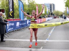 Woman looks joyful as she crosses finishing line in first place. There are no other athletes nearby.