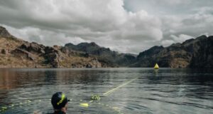 Swimmer in a lake wearing swim cap and goggle looks into the distance towards mountains along a projected straight line