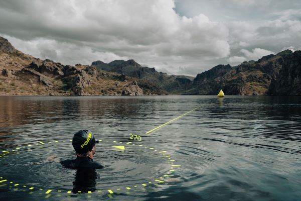 Swimmer in a lake wearing swim cap and goggle looks into the distance towards mountains along a projected straight line