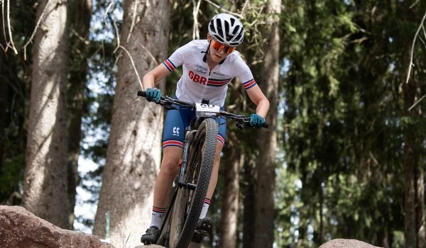 Female cyclist is about to ride off a rock in a forest on a mountain bike