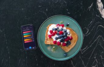 A plate of berries and natural yoghurt on toast next to a phone with a nutrition app on it