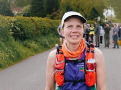 Lady in cap, running clothes and running hydration vest smiles at camera. She is wearing a race number, 438