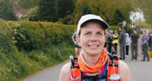 Lady in cap, running clothes and running hydration vest smiles at camera. She is wearing a race number, 438