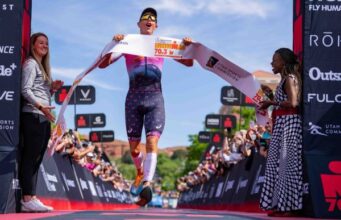 Triathlete crosses the finish line with finish tape in hand looking absolutely thrilled
