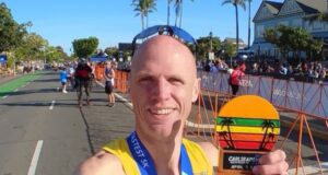 Man in yellow vest and sunglasses holds a medal which says 3rd Place masters