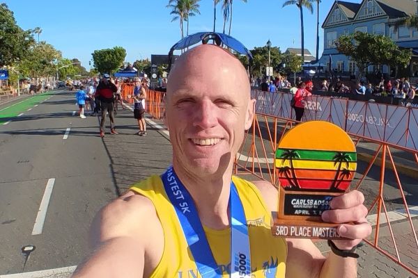 Man in yellow vest and sunglasses holds a medal which says 3rd Place masters