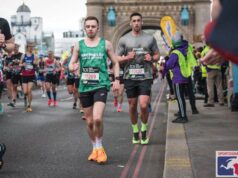 Young man in a Macmillan green vest, black shorts and orange trainers runs across Tower Bridge on the London Marathon