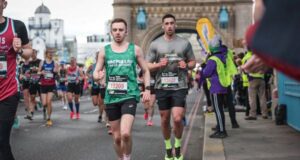 Young man in a Macmillan green vest, black shorts and orange trainers runs across Tower Bridge on the London Marathon