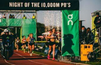 Female athletes on a track run under a gantry with the wording Night of the 10,000M PB's
