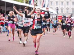 Woman in black club kit raises arms in triumph along the Mall, with Buckingham Palace and other runners visible in the background.