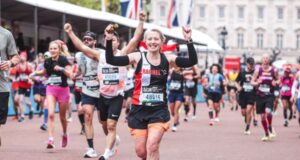 Woman in black club kit raises arms in triumph along the Mall, with Buckingham Palace and other runners visible in the background.