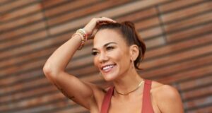 Woman in rust coloured vest with dark hair in ponytail, smiling