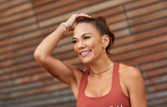 Woman in rust coloured vest with dark hair in ponytail, smiling