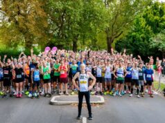 A runner stands in front of a large crowd of runners who are all cheering
