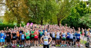 A runner stands in front of a large crowd of runners who are all cheering