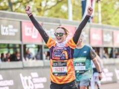 Female runner holds arms in air in joy as she approaches finish line of London Marathon