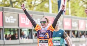 Female runner holds arms in air in joy as she approaches finish line of London Marathon