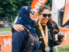 Two female finishers of a Threshold trail series event stand at the finish area with medal around their neck and drink in hand.
