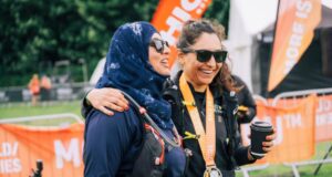 Two female finishers of a Threshold trail series event stand at the finish area with medal around their neck and drink in hand.