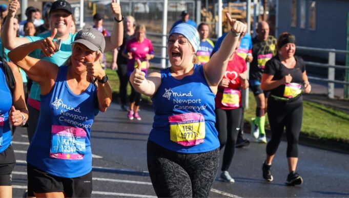 Two runners wearing mind running vests holding their thumbs up for the camera whilst running