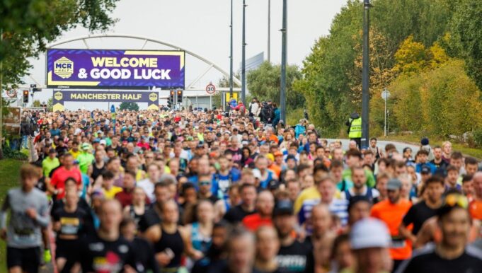 start of the manchester half marathon 2024. Lots of runners heading out on to the course with a large good luck banner in the background