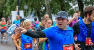 Male runner in blue top tosses water bottle into a blue bin