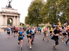 Runners run through a large marble arch with a decorative statue on top