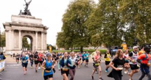 Runners run through a large marble arch with a decorative statue on top