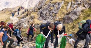 A group pf people carrying green litter bags and litter pickers climb a mountain