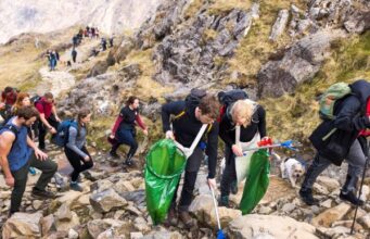 A group pf people carrying green litter bags and litter pickers climb a mountain