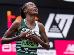 Woman clasps hands to heart in joy. She's wearing a running vest with HASSAN printed on her number.