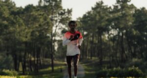 Male athlete runs towards camera on a tree lined road