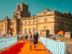 Triathletes run through a transition area with bikes in front of a spectacular palace
