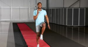 Young man does some running drills on a long red strip of running track inside a building