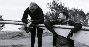 Two men lean over a metal gate, they look tired but elated