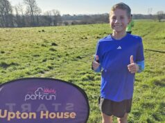 Boy in blue tshirt poses with thumbs up, next to sign saying Upton House.