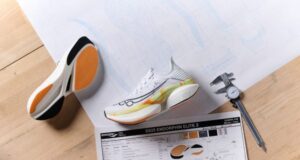 White, ornage and yellow running shoes on a wooden table with a sheet showing all the spec of the shoes