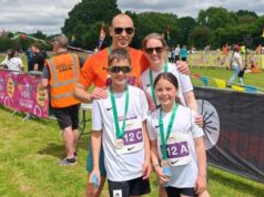Family of four people, man, woman, boy and girl, smile, wearing running medals.