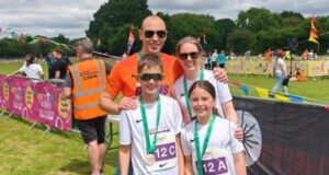 Family of four people, man, woman, boy and girl, smile, wearing running medals.