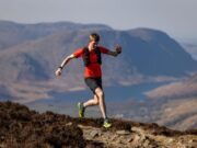 Man in red t-shirt and black shorts runs on a high mountain path