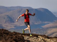 Man in red t-shirt and black shorts runs on a high mountain path