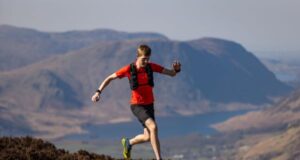 Man in red t-shirt and black shorts runs on a high mountain path