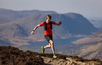 Man in red t-shirt and black shorts runs on a high mountain path