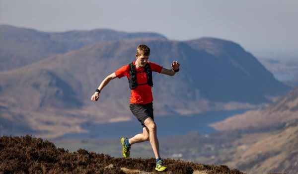 Man in red t-shirt and black shorts runs on a high mountain path