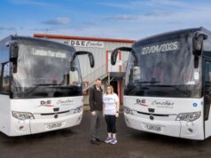 A man and a woman stand in front of two coaches at a depot