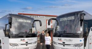 A man and a woman stand in front of two coaches at a depot